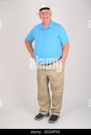 Der Mann steht mit Händen auf den Hüften. Er trägt ein blaues Poloshirt und Khaki-Hosen. Weißer Panamahut und dunkle Schuhe runden sein Outfit ab. Sein Lächeln fühlt sich entspannt an Stockfoto