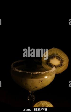 Kiwi-Cocktail mit gesalzenem Rand und frischer Kiwi-Scheibe auf dunklem Hintergrund. Das Studio in Nahaufnahme betont lebendiges Grün, elegantes Design und Refre Stockfoto
