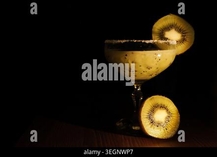 Kiwi-Smoothie-Cocktail mit Chiasamen in einem Margarita-Glas, garniert mit einer Kiwi-Scheibe und Zuckerrand, auf einer Holzoberfläche gegen eine dunkle bac Stockfoto