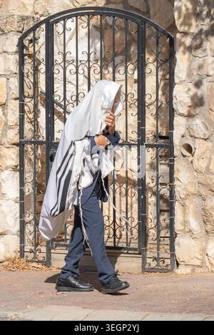 Ein religiöser jüdischer Mann, der eine Jerusalem-Straße hinuntergeht, in einen Gebetschal gewickelt. Stockfoto