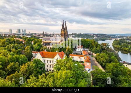 Das Morgenlicht taucht die Vysehrader Basilika St. Peter und St. Paul in goldene Farbtöne. Umgeben von üppigem Grün steht die historische Kirche hoch, während die Stadt erwacht. Stockfoto