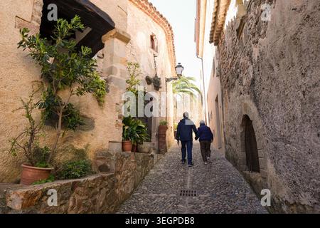Ein Paar, das durch eine enge, kopfsteingepflasterte Gasse im historischen Stadtteil Vila Vella in Tossa de Mar, Spanien, spaziert Stockfoto