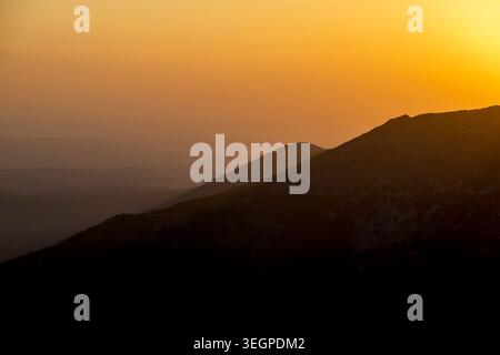 Eine malerische Landschaft, die die dunklen, geschichteten Silhouetten von Bergkämmen unter einem warmen goldenen und orangen Sonnenuntergangshimmel zeigt, Peña de Francia, Salamanca, Spai Stockfoto