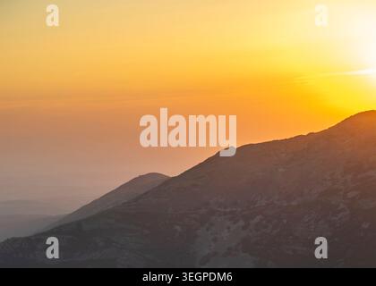 Eine malerische Landschaft, die die dunklen, geschichteten Silhouetten von Bergkämmen unter einem warmen goldenen und orangen Sonnenuntergangshimmel zeigt, Peña de Francia, Salamanca, Spai Stockfoto