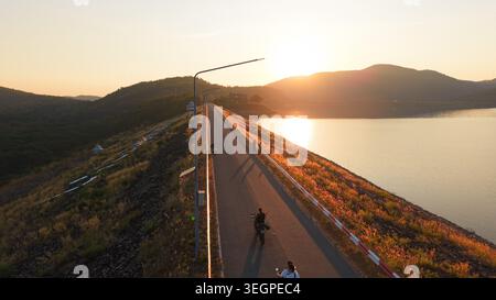 Menschen, die Motorräder auf der Mae kuang Damm Road fahren und den Sonnenuntergang in der goldenen Stunde genießen Stockfoto