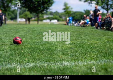 Fußball rollt während eines Spiels in einem Park auf dem Gras, während die Zuschauer an einem sonnigen Tag im Hintergrund zusehen Stockfoto