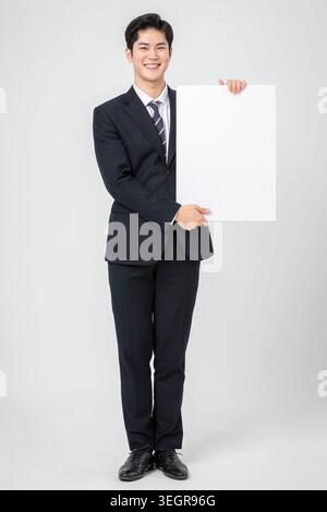 Ein junger asiatischer Profi im Business-Anzug hält ein weißes Schild. Stockfoto