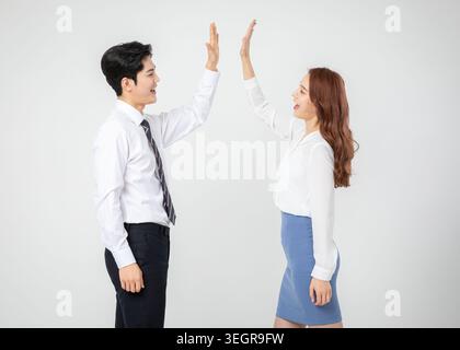 Ein junges asiatisches Geschäftspaar steht einander gegenüber, lächelnd und hochmütig in einem neutralen weißen Hintergrund. Stockfoto