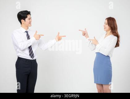 Ein junger asiatischer Mann und eine junge asiatische Frau, beide in Geschäftskleidung gekleidet, zeigen einander mit einem freundlichen, lächelnden Ausdruck. Stockfoto