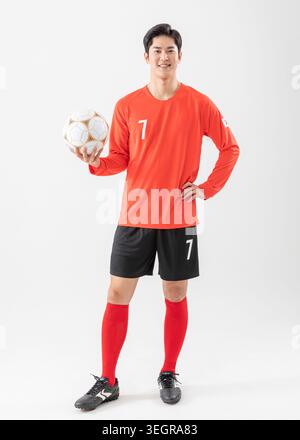 Ein junger männlicher Fußballspieler in Uniform hält einen Fußball. Stockfoto