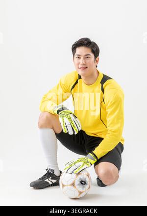 Ein männlicher Fußballspieler kniet vor einem Fußball, trägt eine gelbe und schwarze Uniform. Stockfoto