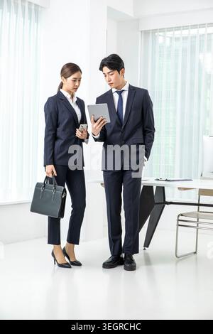 Ein junger asiatischer Geschäftsmann und eine junge asiatische Geschäftsfrau in einem modernen Büro, die gemeinsam ein Tablet überprüfen. Stockfoto