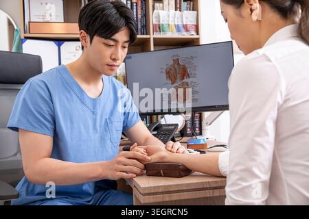 Ein Arzt in blauer Uniform kontrolliert den Blutdruck eines Patienten an einem Schreibtisch in einer modernen Arztpraxis. Stockfoto