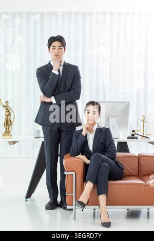 Ein junger asiatischer Mann und eine junge Frau in Geschäftskleidung sitzen in einem modernen Büro und führen ein professionelles Gespräch. Stockfoto