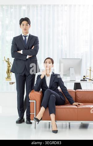 Zwei Geschäftsleute, ein Mann und eine Frau, stehen selbstbewusst in einer modernen Anwaltskanzlei und untersuchen ihre Umgebung. Stockfoto