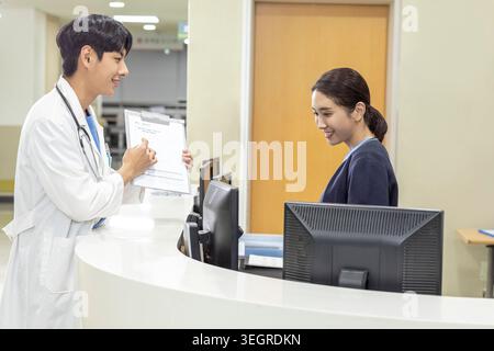 Ein Arzt überreicht einem Patienten einen medizinischen Bericht, in einem Krankenhausaufnahmebereich. Stockfoto