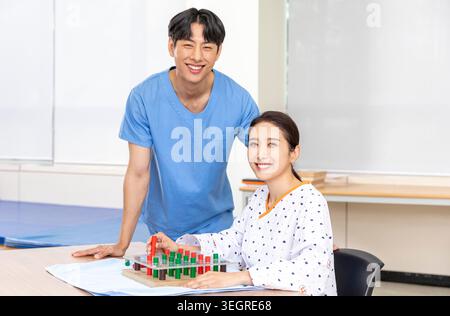 Zwei junge Ärzte lächeln und arbeiten zusammen in einem Krankenhausklassenzimmer, um Patienten mit einem Brettspiel über medizinische Behandlungen zu unterrichten. Stockfoto