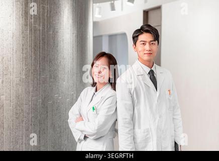Zwei Ärzte in weißen Labormänteln stehen in einem Krankenhausflur und lächeln in die Kamera. Stockfoto