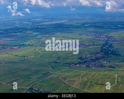 Blick aus der Vogelperspektive auf üppig grüne Weinberge und kleine Dörfer, die sich über die sanfte Landschaft unter einem bewölkten Himmel in Ribeauville, Grand Est, Frankreich verteilen. Stockfoto
