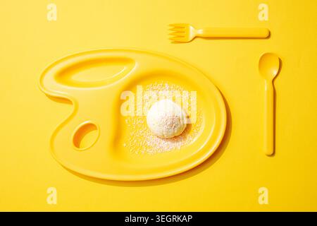 Ein einzelner Messlöffel Vanilleeis auf einer gelben Farbpalette. Stockfoto
