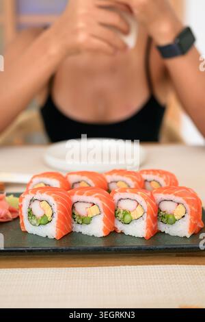 Frische Lachs-Maki-Sushi-Brötchen mit Krabbenstab, Gurke, Ei und Spargel-Füllung, wunderschön serviert mit eingelegtem Ingwer auf einer dunklen Keramikplatte. Stockfoto