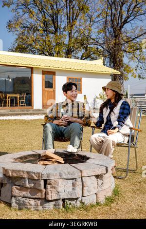Zwei Freunde sitzen am Lagerfeuer und trinken Bier und Marshmallows in einem sonnigen Hinterhof. Stockfoto