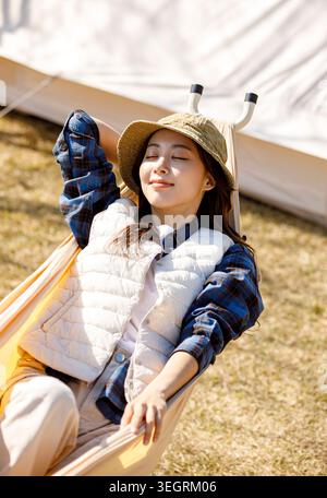 Eine junge Frau entspannt sich in einer Hängematte und genießt die warme Sonne auf einem grasbewachsenen Rasen. Stockfoto