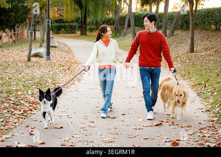 Ein Paar geht Hand in Hand mit ihren Hunden in einem Park an einem sonnigen Tag. Stockfoto