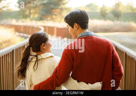 Ein junges Paar spaziert Hand in Hand auf einem gewundenen Waldweg und genießt die Ruhe der natürlichen Umgebung. Stockfoto