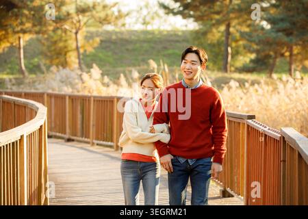 Ein junges Paar geht Hand in Hand durch einen sonnigen Wald, lacht und genießt die Gesellschaft des anderen. Stockfoto