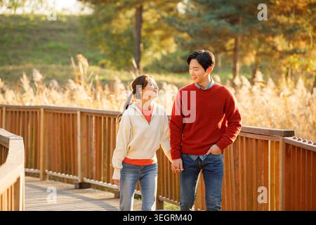 Ein junges Paar geht Hand in Hand auf einer Holzbrücke durch einen sonnigen Wald. Stockfoto