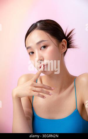 Eine junge asiatische Frau berührt ihre Lippen mit dem Zeigefinger und blickt mit einem nachdenklichen Ausdruck in die Kamera. Stockfoto