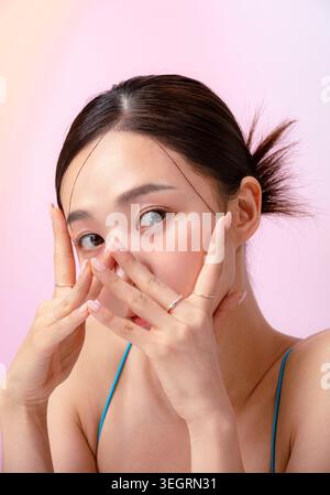 Eine junge Frau berührt ihr Gesicht mit ihren Händen und blickt direkt in die Kamera. Stockfoto