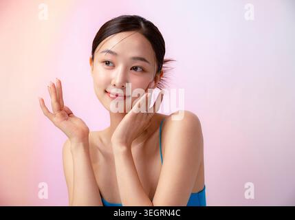 Eine junge asiatische Frau mit den Händen auf den Wangen, lächelt und blickt direkt in die Kamera. Stockfoto