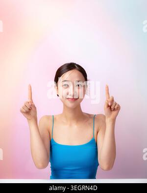 Eine junge Frau in einem blauen Tank zeigt mit beiden Zeigefingern nach oben. Stockfoto