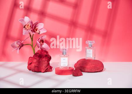 Eine Auswahl an Parfümflaschen und Blumen auf einem weißen Tisch vor rotem Hintergrund. Stockfoto