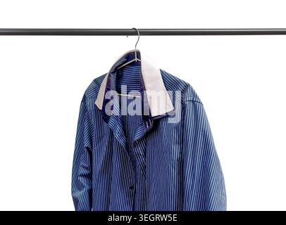 Gestreiftes Hemd, das am Aufhänger unter der Schiene hängt. Kleidungsstück hängt auf dem Regal. Auswahl von Männerbekleidung. Stockfoto