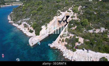 Aus der Vogelperspektive auf die jugoslawische Armee unterirdische Bootsunterkunft Potkop Parja, die in die felsige Küste mit türkisfarbenem Wasser und üppigem Grün in Rogac gehauen wurde Stockfoto