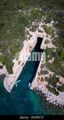 Aus der Vogelperspektive auf die jugoslawische Armee unterirdische Bootsunterkunft Potkop Parja mit türkisfarbenem Wasser und üppiger grüner Vegetation in Rogacic, Splitsko-dalmatinska Stockfoto