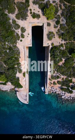 Aus der Vogelperspektive auf die jugoslawische Armee unterirdische Bootsunterkunft Potkop Parja mit türkisfarbenem Wasser und Paddleboardern am Eingang in Rogacic, Splitsko-da Stockfoto