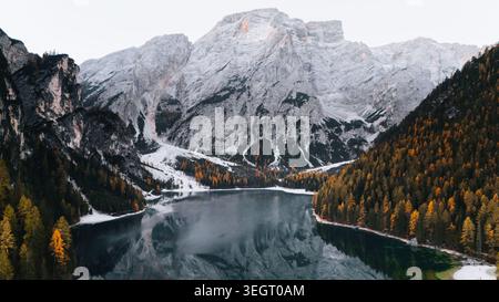 Aus der Vogelperspektive auf den Pragser See, umgeben von schneebedeckten Berggipfeln und dichten Wäldern mit herbstlichen Farben in Praggs, Trentino-Südtirol, Italien. Stockfoto