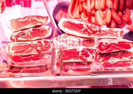 Nahaufnahme der traditionellen spanischen serrano-Schinkenblöcke aus gepökeltem Marmeladen in Plastikfolie, die an einem Metzgerstand auf dem berühmten öffentlichen Markt La Boqueria in B gestapelt wurden Stockfoto