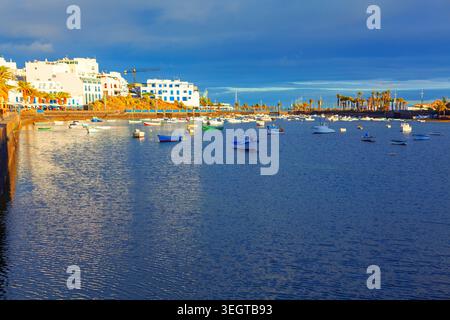 El Charco de San Gines Lagune in Arrecife, Lanzarote, bietet Reihen traditioneller weißer und blauer Gebäude unter einem dramatischen Himmel. Zahlreiche kleine Fische Stockfoto