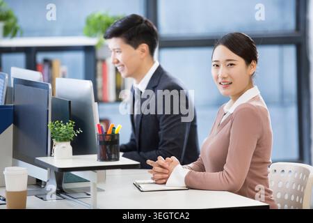 Eine junge asiatische Berufsfrau und ihr männlicher Kollege arbeiten in einem modernen Büro zusammen, lächeln und unterhalten sich. Stockfoto