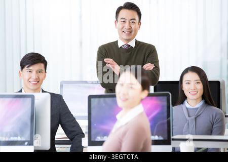 Ein Mann in einem grünen Pullover, der in einem modernen Büro steht und Kollegen im Hintergrund an Computern arbeiten. Stockfoto
