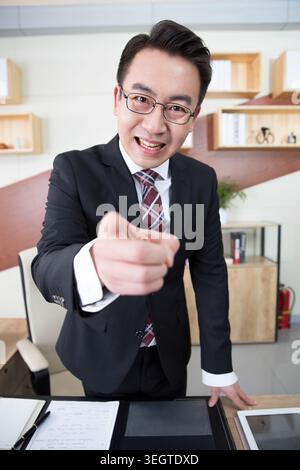 Ein asiatischer Geschäftsmann mittleren Alters in einem Anzug macht Gesten in einem Büro. Stockfoto