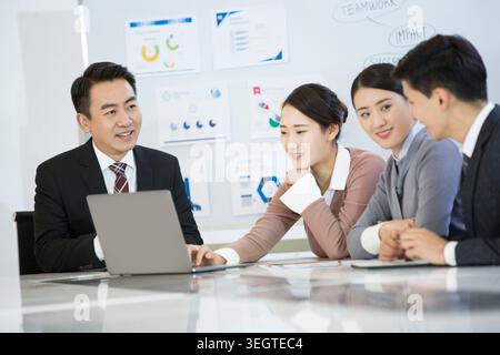 Eine Gruppe verschiedener Geschäftsleute, die an einem Konferenztisch sitzen und gemeinsam an einem Laptop arbeiten. Stockfoto