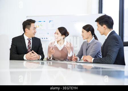 Eine Gruppe asiatischer Kollegen in Geschäftskleidung sitzt an einem Konferenztisch, lacht und diskutiert ein Projekt. Stockfoto