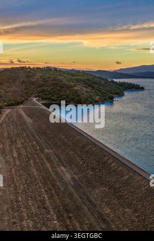 Vertikale Luftaufnahme der Glenbawn Dam Mauer, die zu einem Sonnenuntergang über der umliegenden Bergkette in NSW Australien führt. Drohnenfotografie. Stockfoto