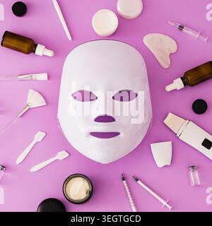 Futuristische Hautpflege-Technologie-Komposition mit LED-Gesichtsmaske und Schönheitswerkzeugen auf violettem Hintergrund. Luxuriöse Hautpflege und Beauty-Konzept. Flache Lagen. Stockfoto